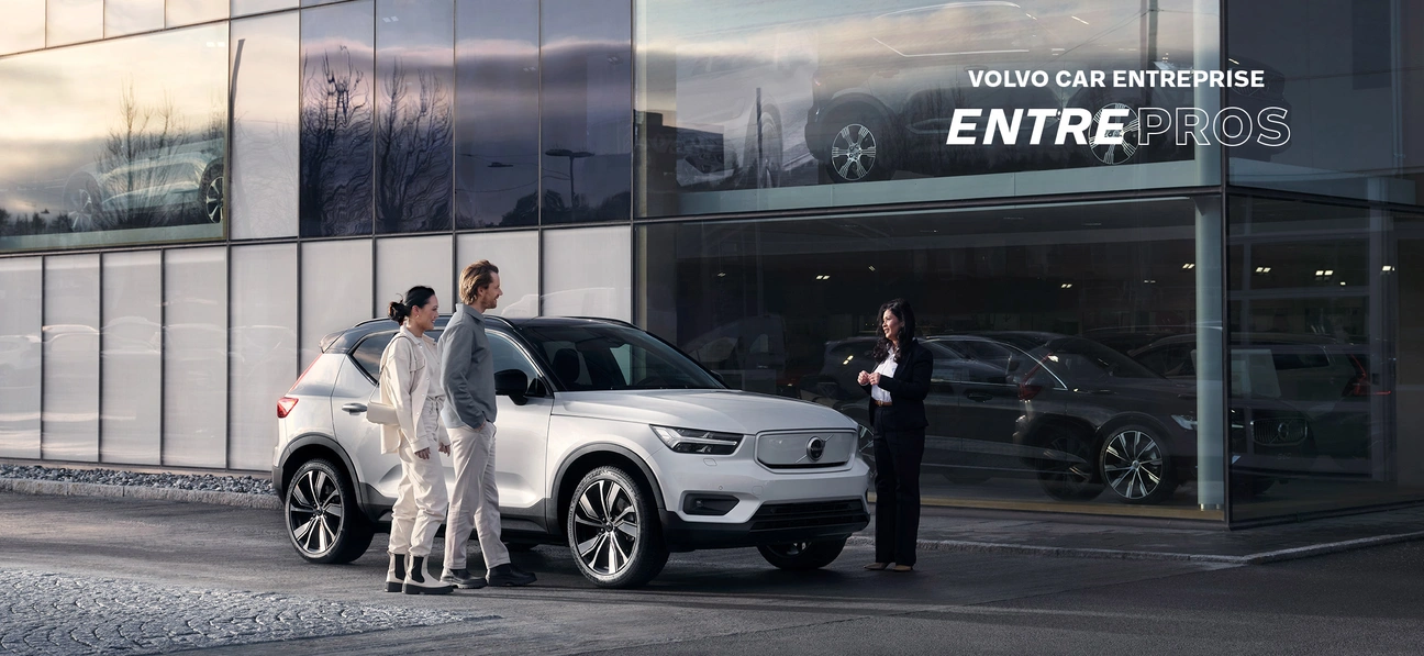 Trois personnes près d’un Volvo XC40 blanc devant un bâtiment vitré avec l’inscription 'VOLVO CAR ENTREPRISE ENTREPROS'