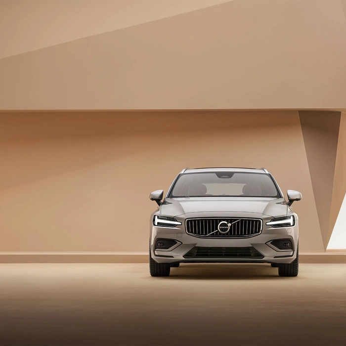 Vue avant d’un Volvo V60 argenté dans un décor beige minimaliste avec éléments architecturaux géométriques