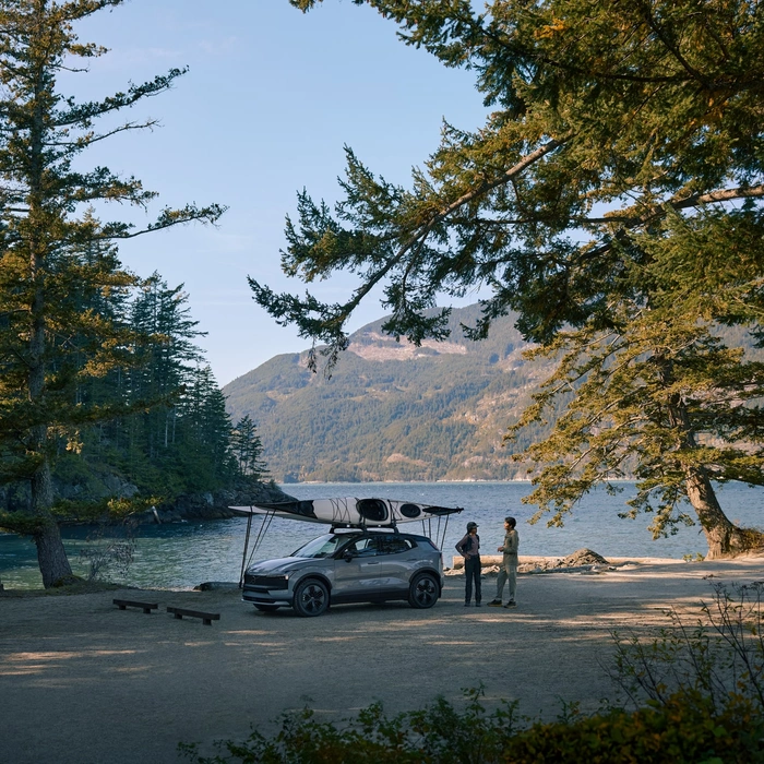 Volvo EX30 Cross Country garé devant un lac avec un kayak sur le toit et deux personnes à côté qui discutent