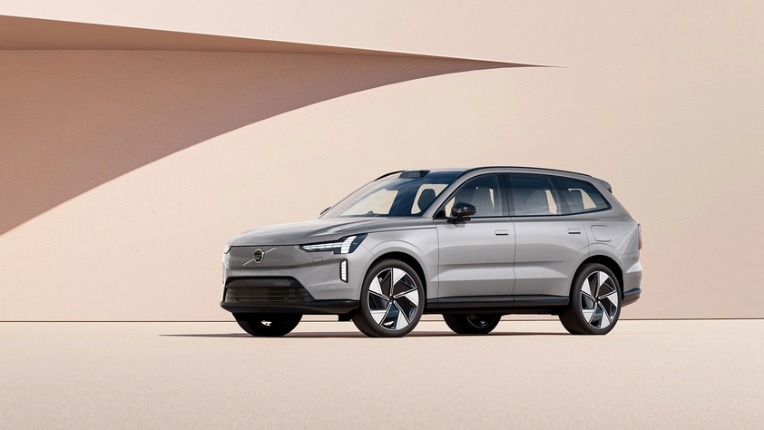 Volvo EX90 argenté garé devant un mur beige avec une ombre projetée