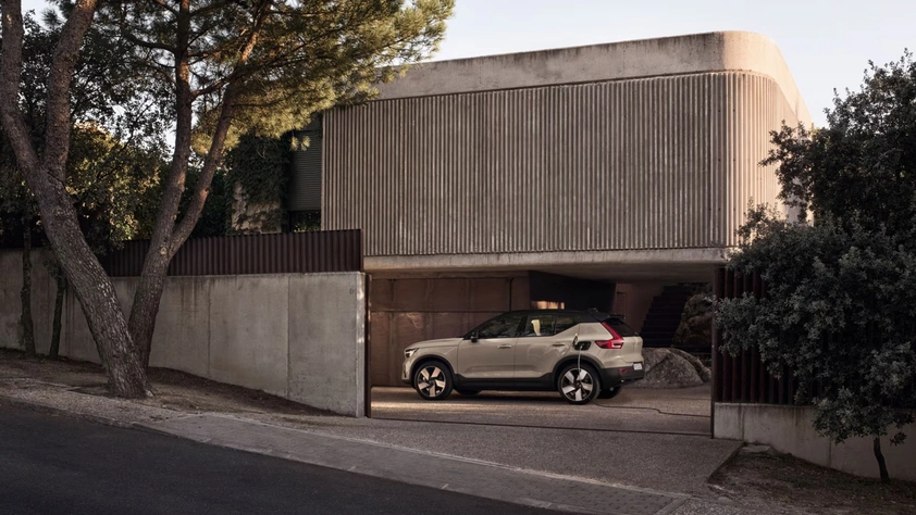 Maison moderne en béton avec un Volvo EX40 argenté garé devant, entourée d’arbres et de verdure