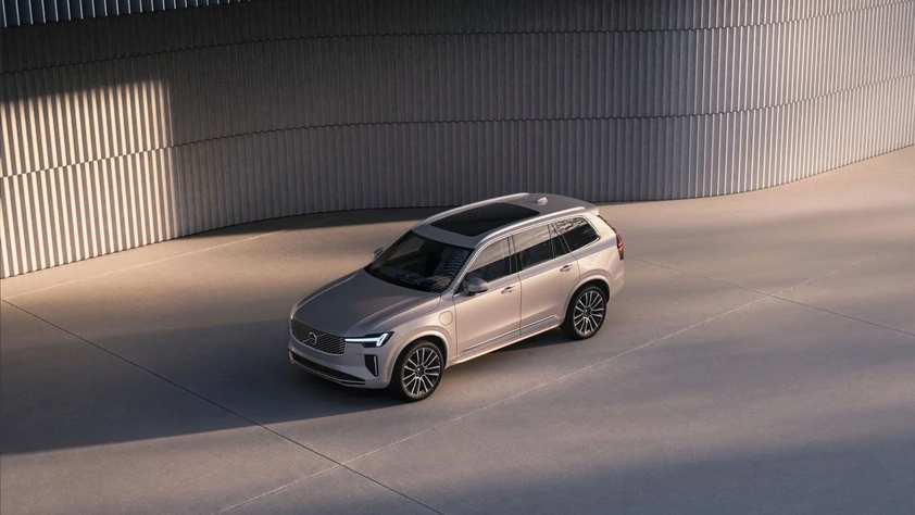 Volvo XC90 argenté garé sur une surface en béton avec un bâtiment moderne et courbé en arrière-plan