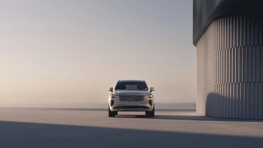 Vue avant d’un Volvo XC90 gris garé près d’un bâtiment cylindrique moderne aux lignes verticales
